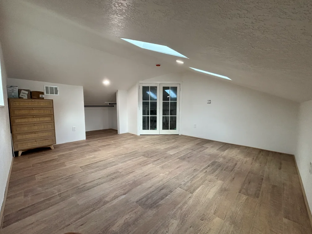 Finished attic room with white walls, windows, skylight, and laminate flooring.