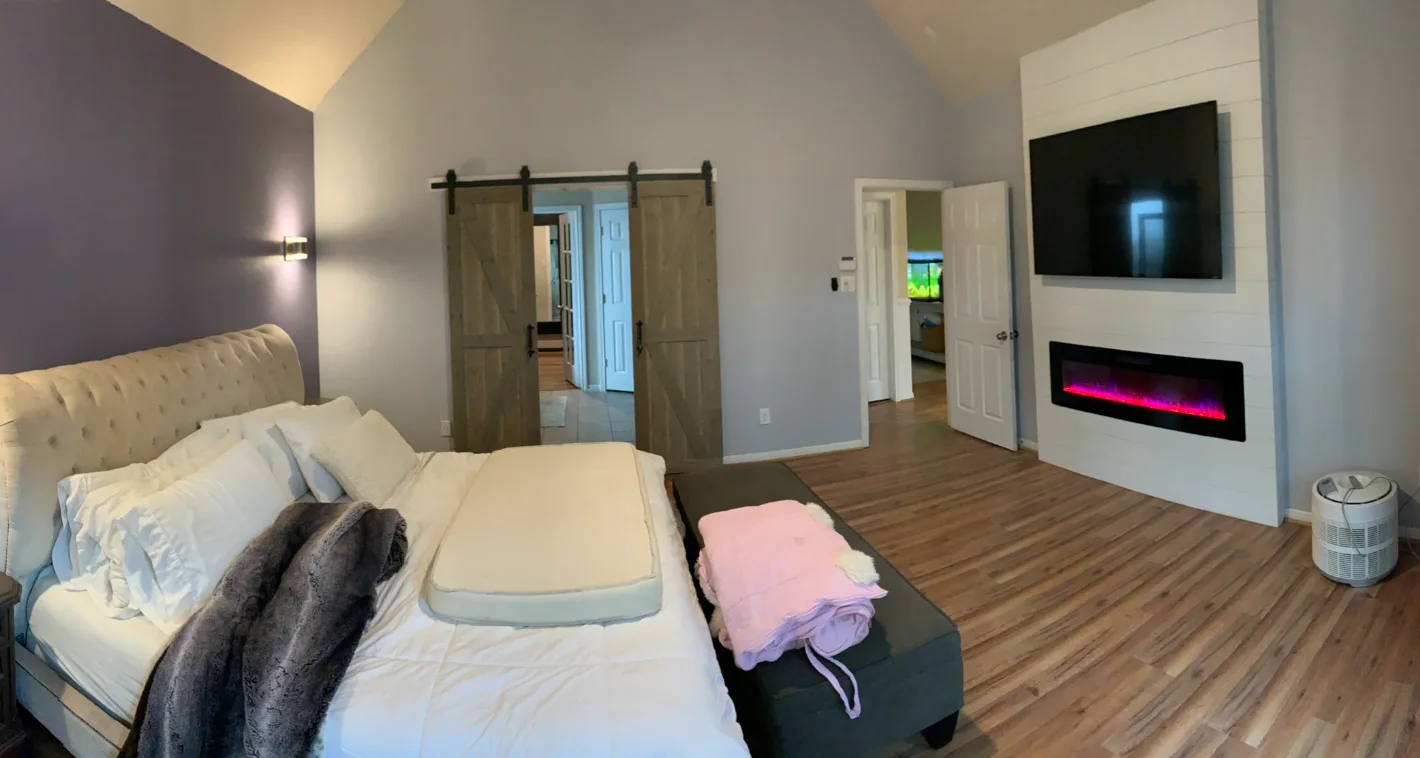 Bedroom with framed French doors, a wall-mounted television, electric fireplace, and laminate flooring.